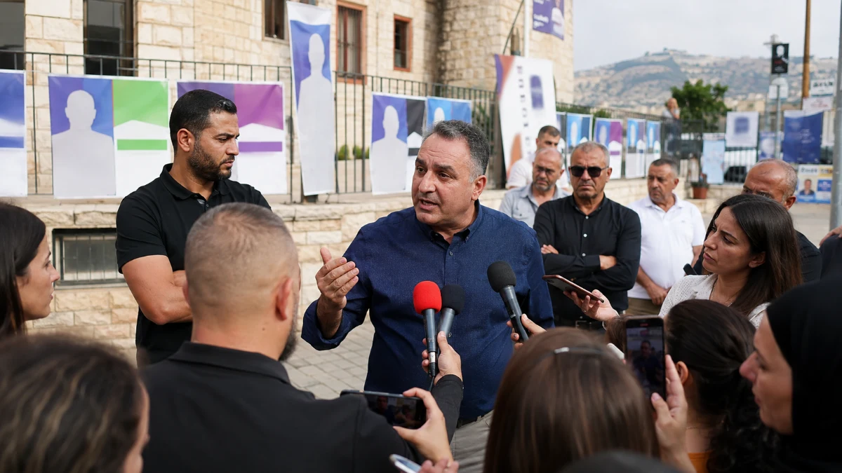 מערכת בחירות מקומית בעוספיה, עם שלטי מועמדים לא מזוהים ודיון ציבורי על התנהלות המועצה