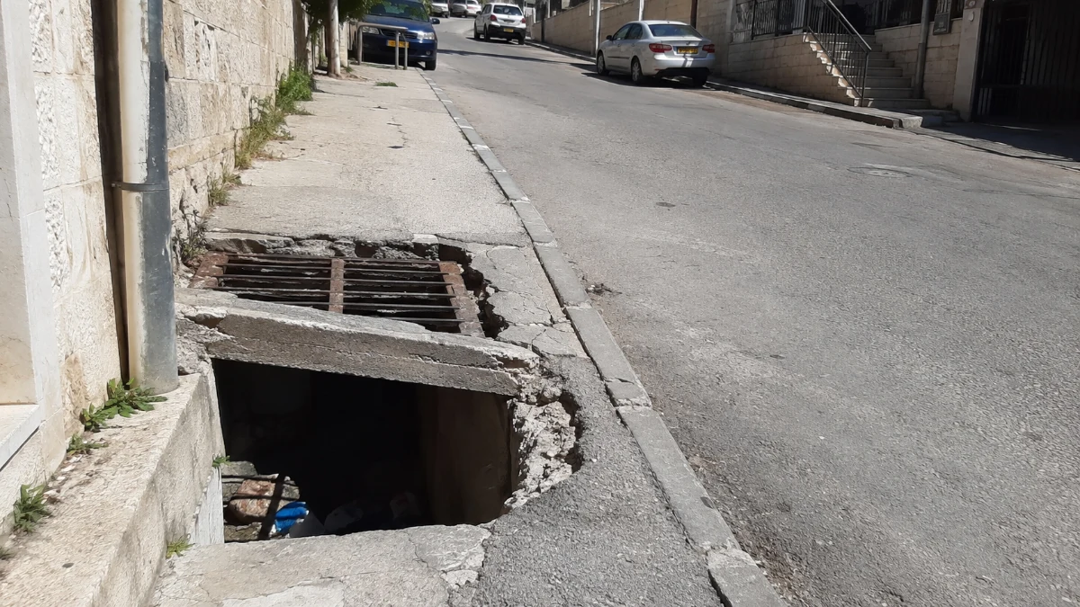 פתח ניקוז שבור בקצהו בכביש בשכונת צור באהר בירושלים, במראה רחוב עירוני באור יום