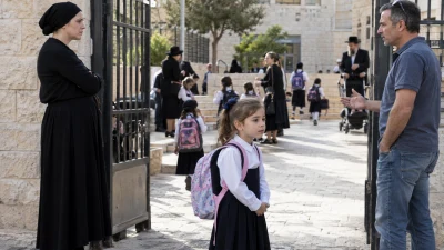 ילדה עם תיק בית ספר בכניסה למסגרת חינוך חרדית, כששני הוריה עומדים ברקע ללא פרטים מזהים